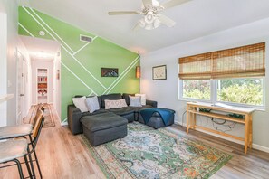 A living room with a sectional sofa, a coffee table, a rug, and a window with blinds. - Mid-century Gainesville Getaway: 3 Mi to UF Campus (Gainesville)