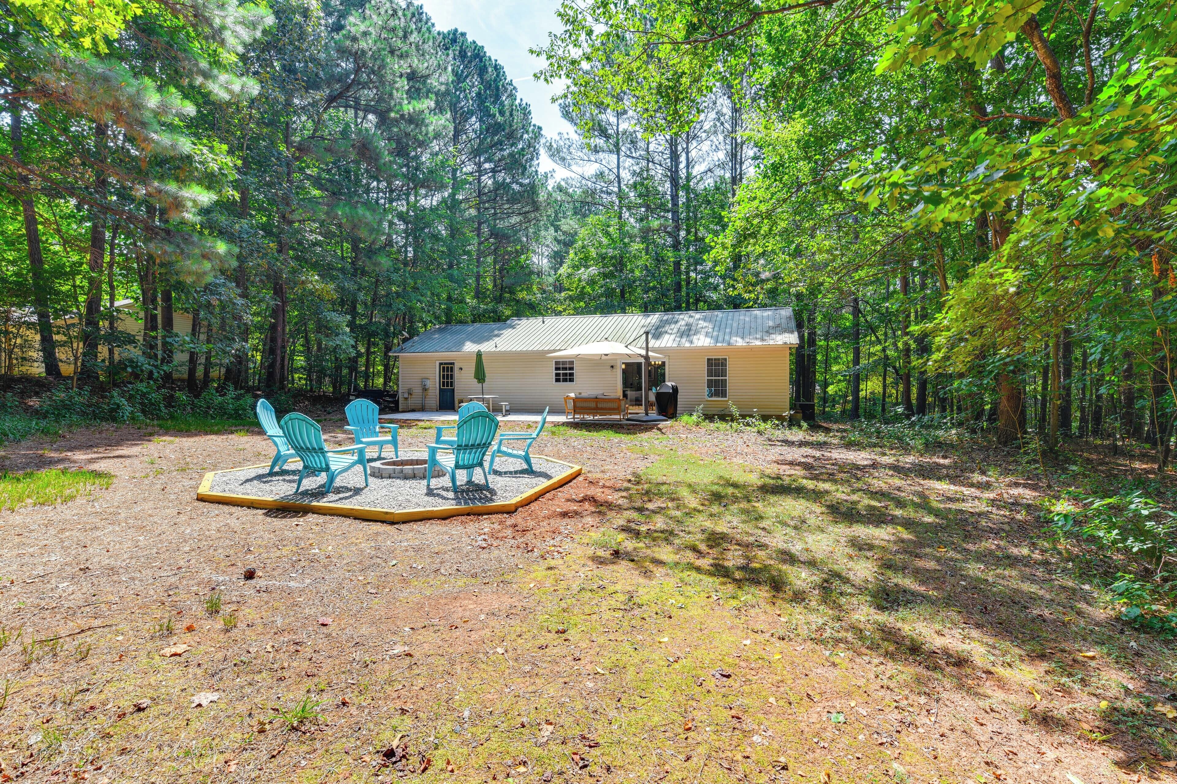 A rustic cabin surrounded by dense forest, with a gravel patio and outdoor seating.