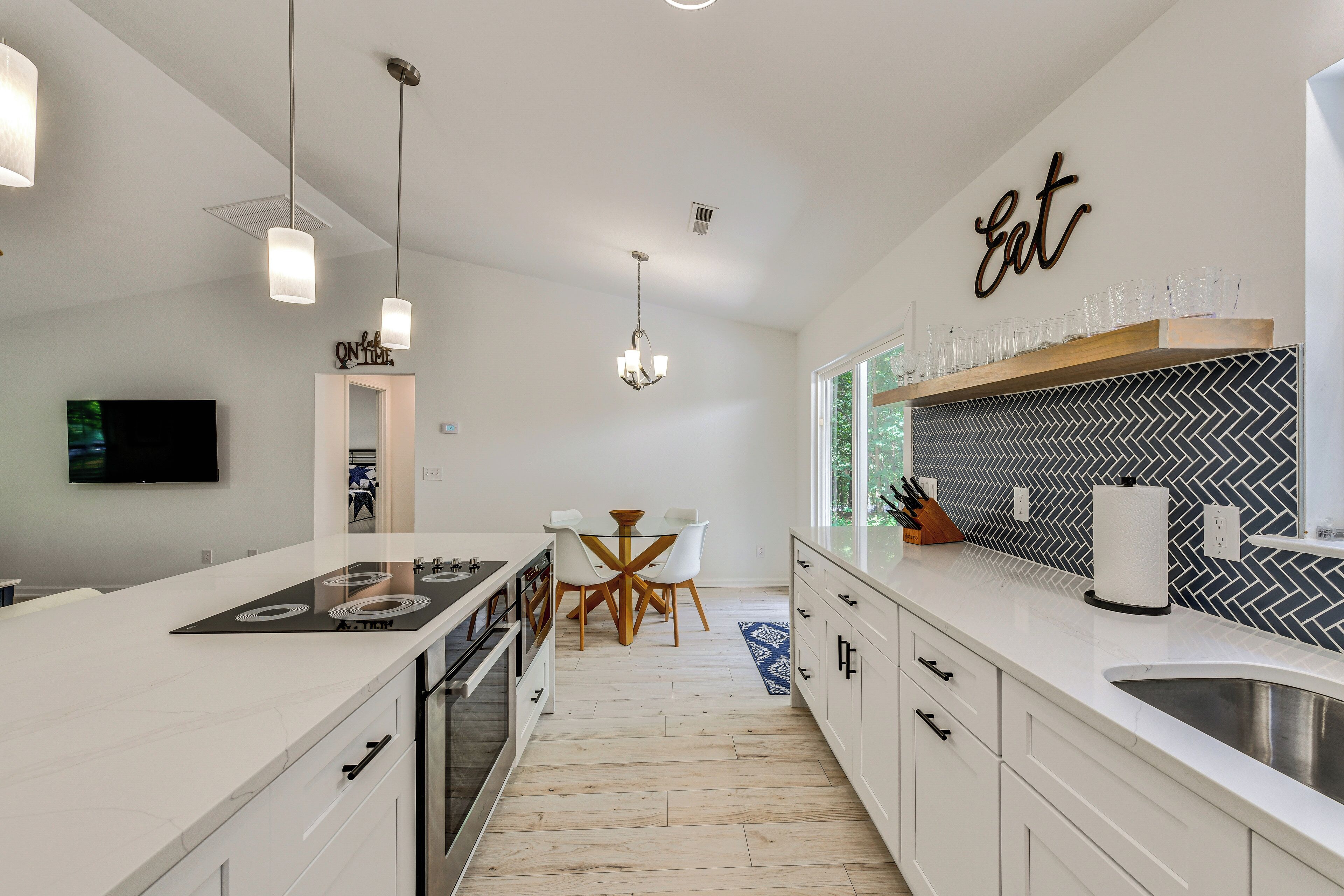 A modern kitchen with white cabinetry, a central island, pendant lighting, and a herringbone-patterned backsplash.