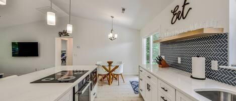 A modern kitchen with white cabinetry, a central island, pendant lighting, and a herringbone-patterned backsplash.