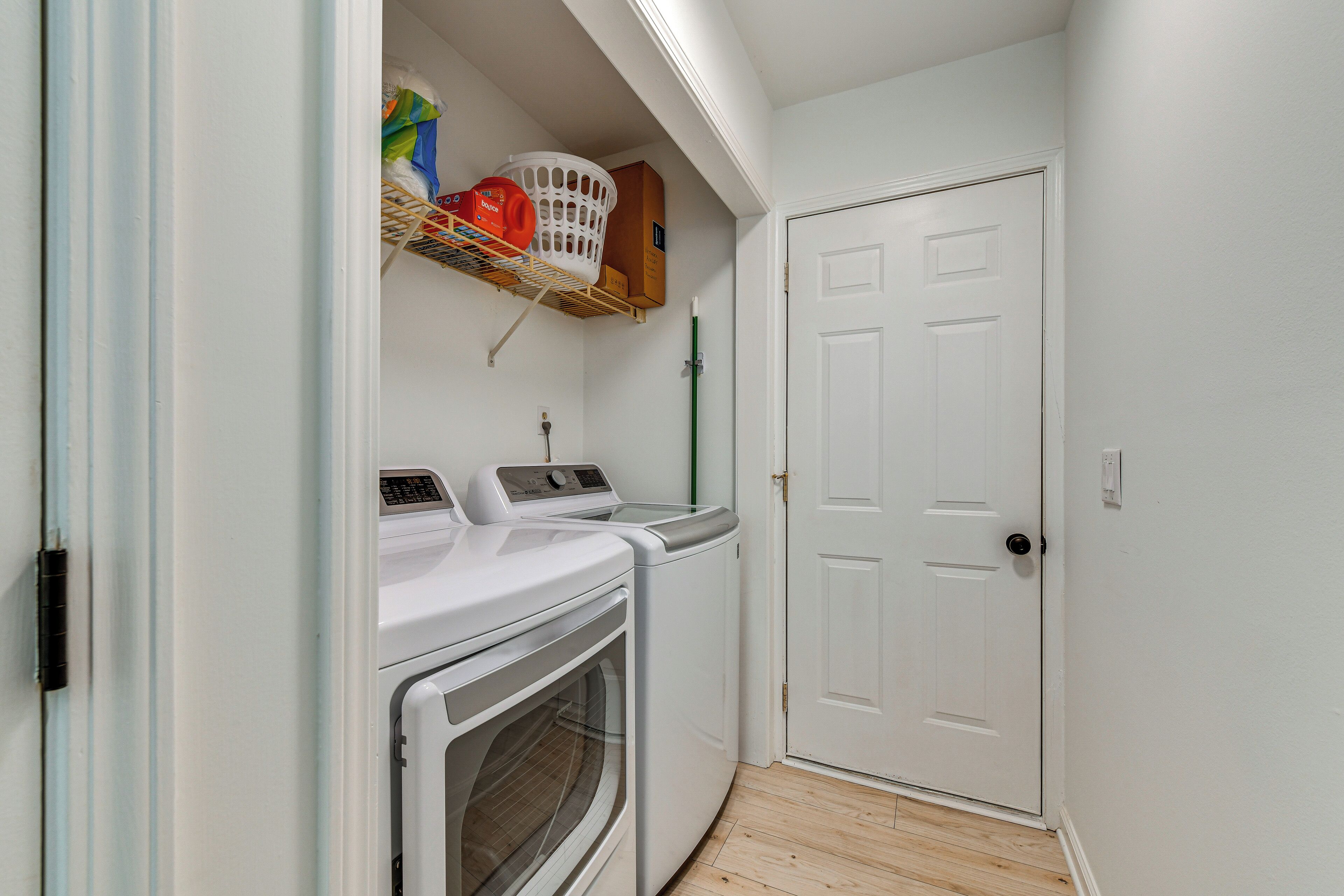 A laundry room with a washing machine, dryer, and a shelf with baskets and cleaning supplies.