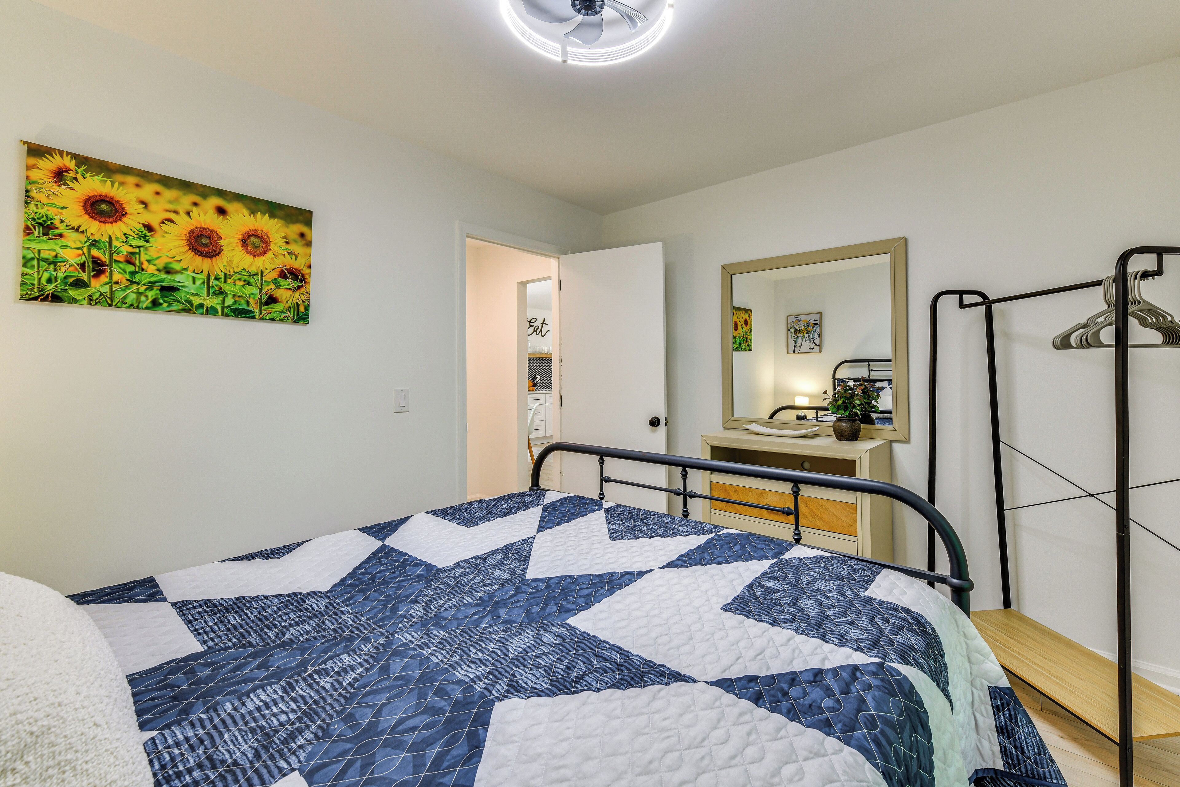 Un dormitorio con una cama, un espejo y un cuadro de girasoles.