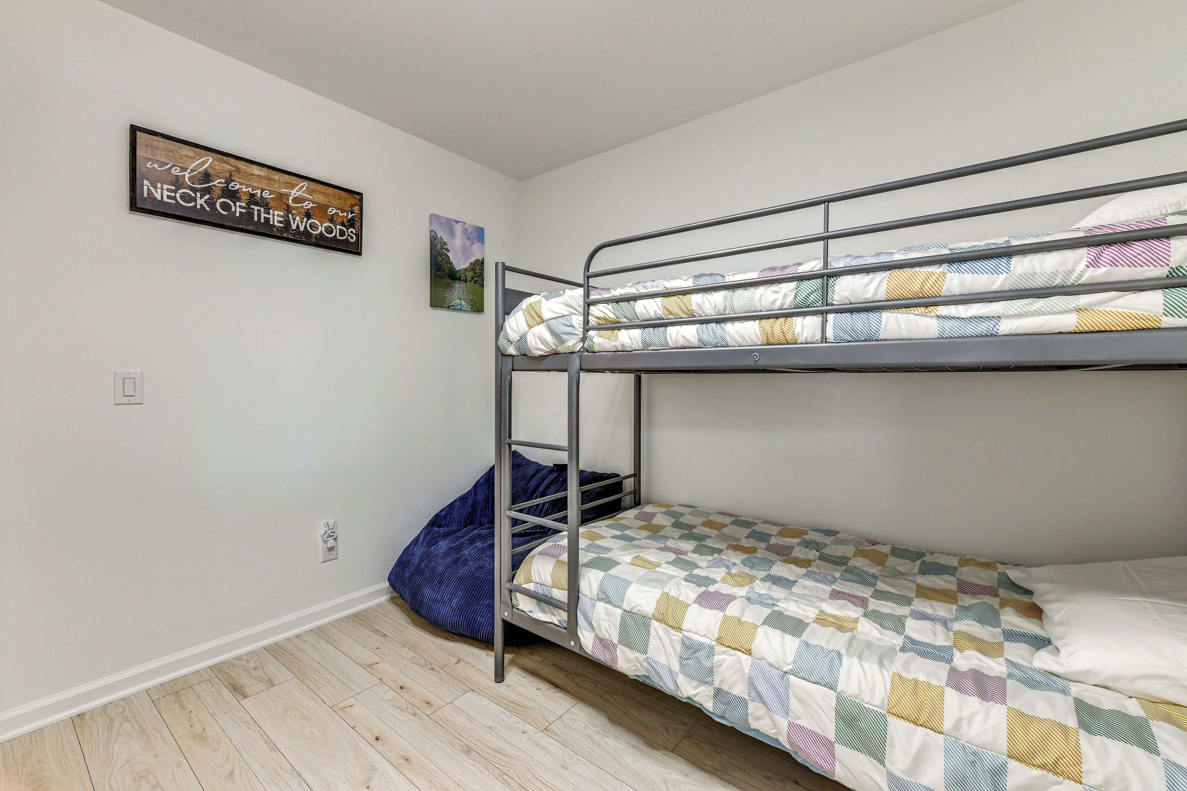 A bunk bed room with a welcome sign, a framed picture, and a wooden floor.