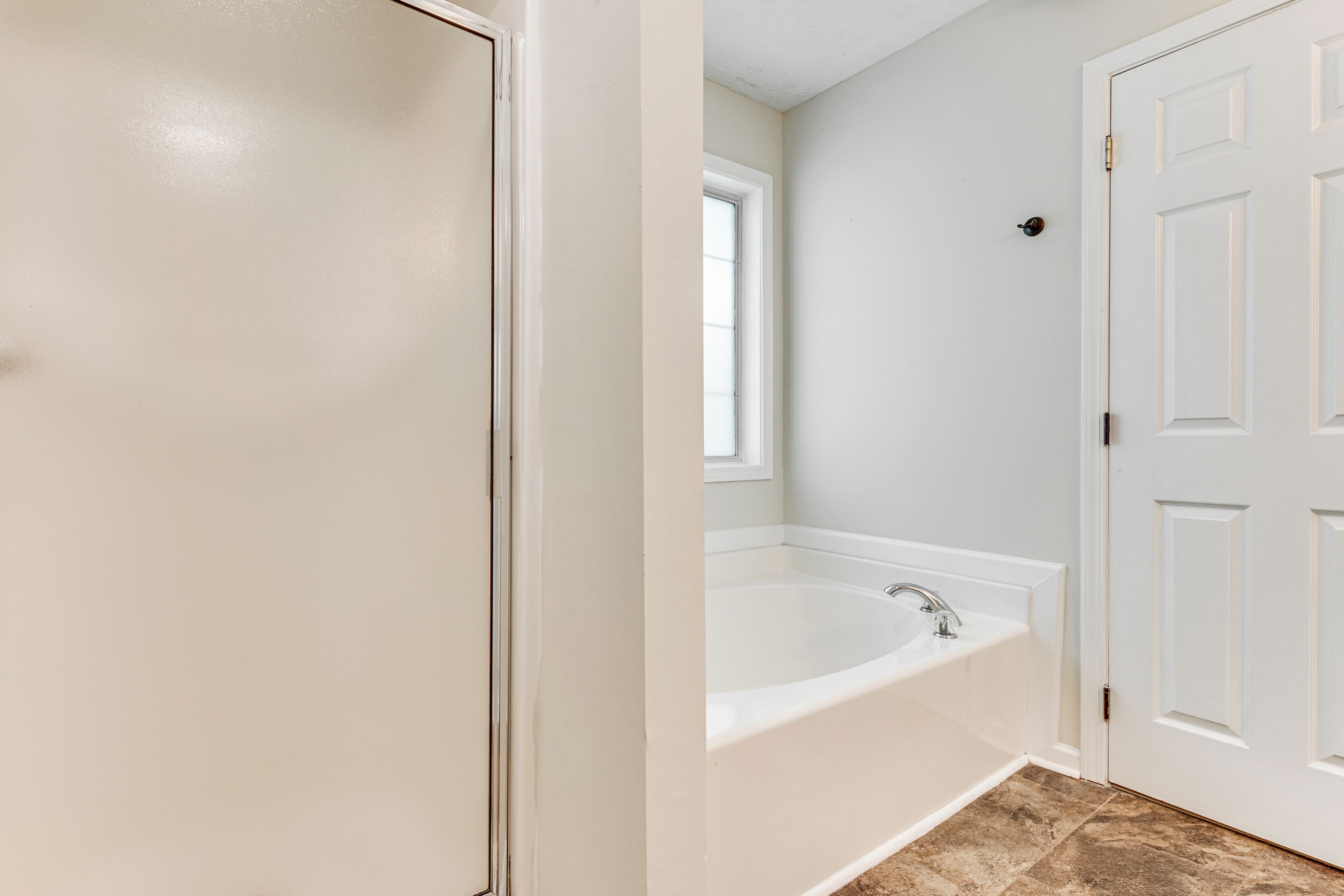 A bathroom with a white bathtub, a window, and a white door.