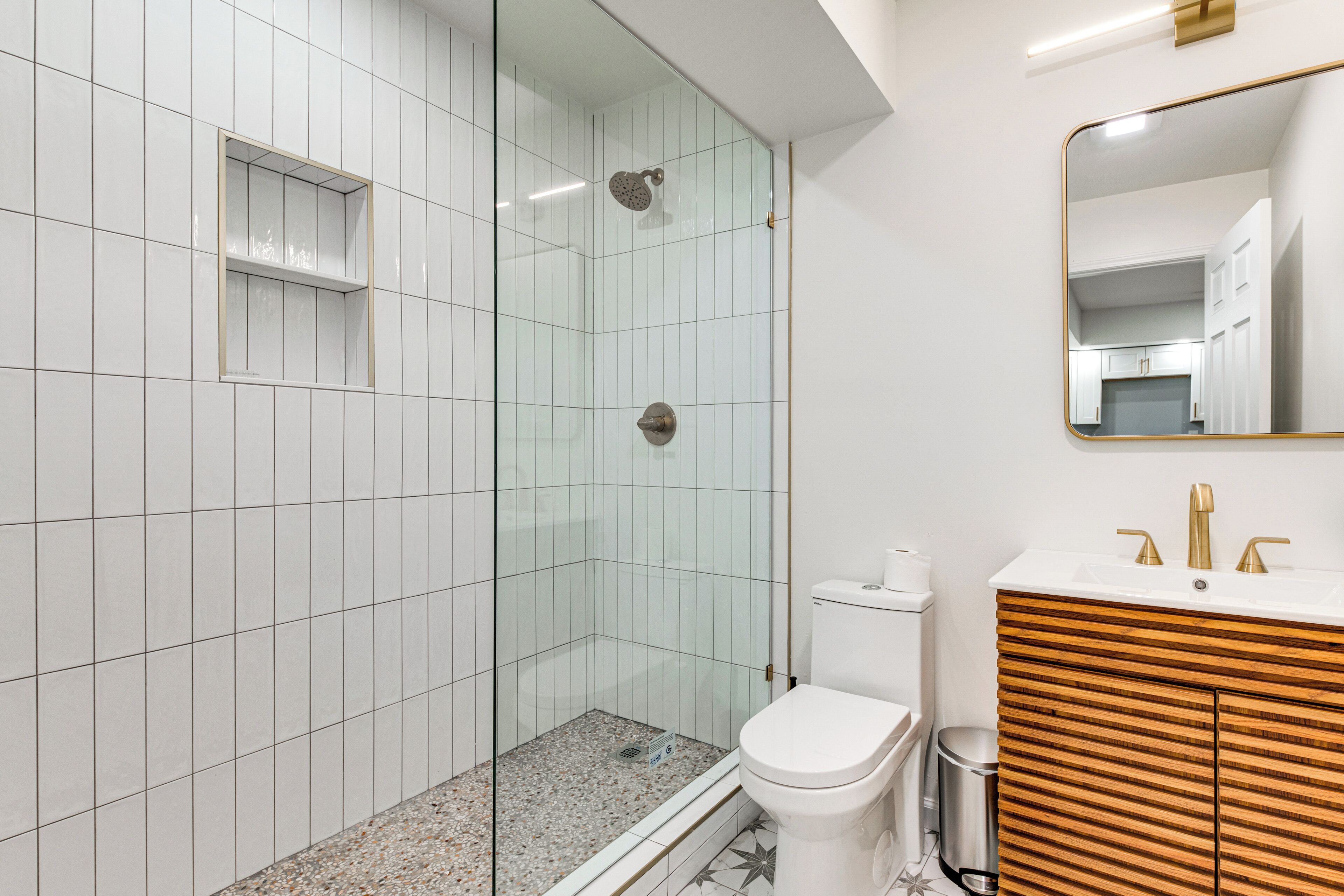Ein modernes Badezimmer mit einer Duschkabine, einer weißen Toilette und einem Holzbadezimmer-Möbel mit Spiegel.