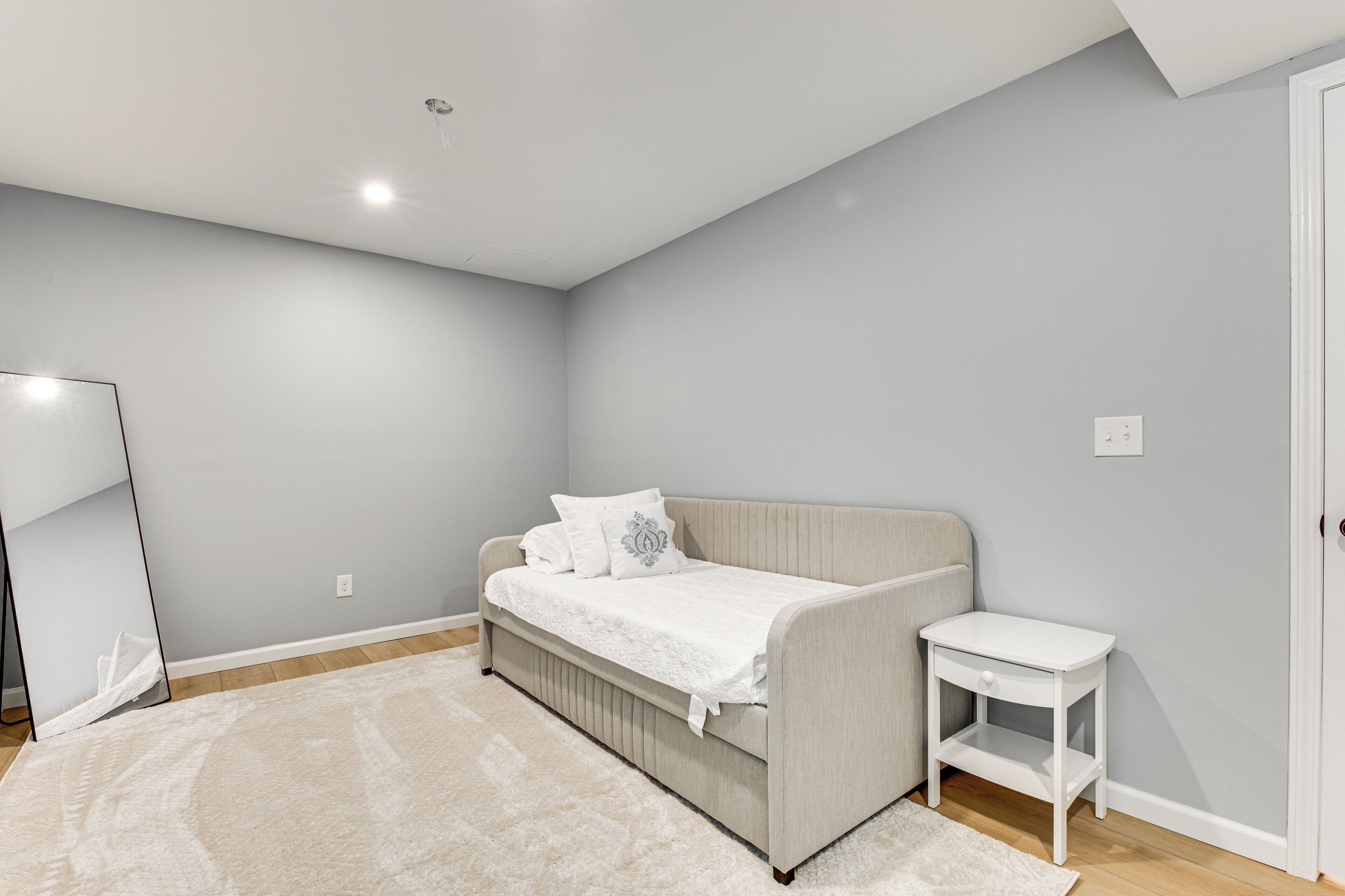 A bedroom with a bed, a bedside table, a mirror, and a light switch on the wall.