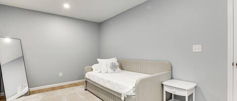 A bedroom with a bed, a bedside table, a mirror, and a light switch on the wall.