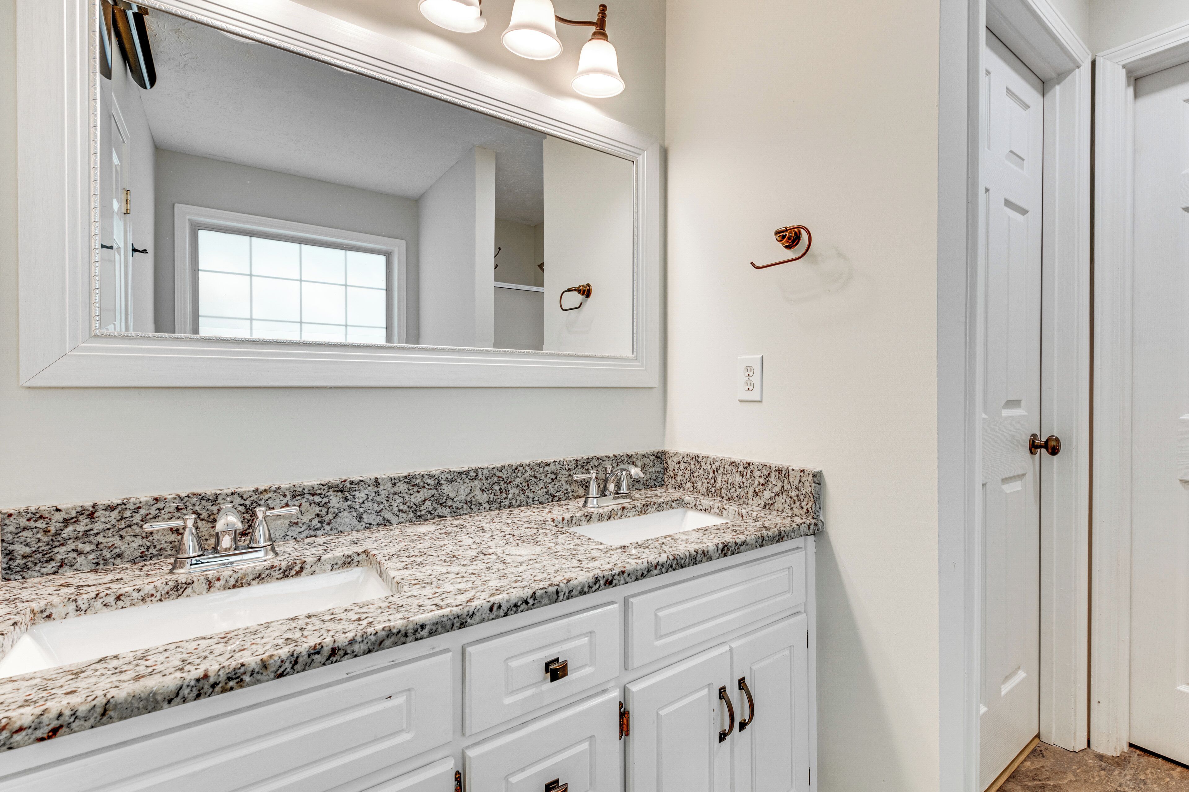 A bathroom with a double sink, a large mirror, and white cabinetry.