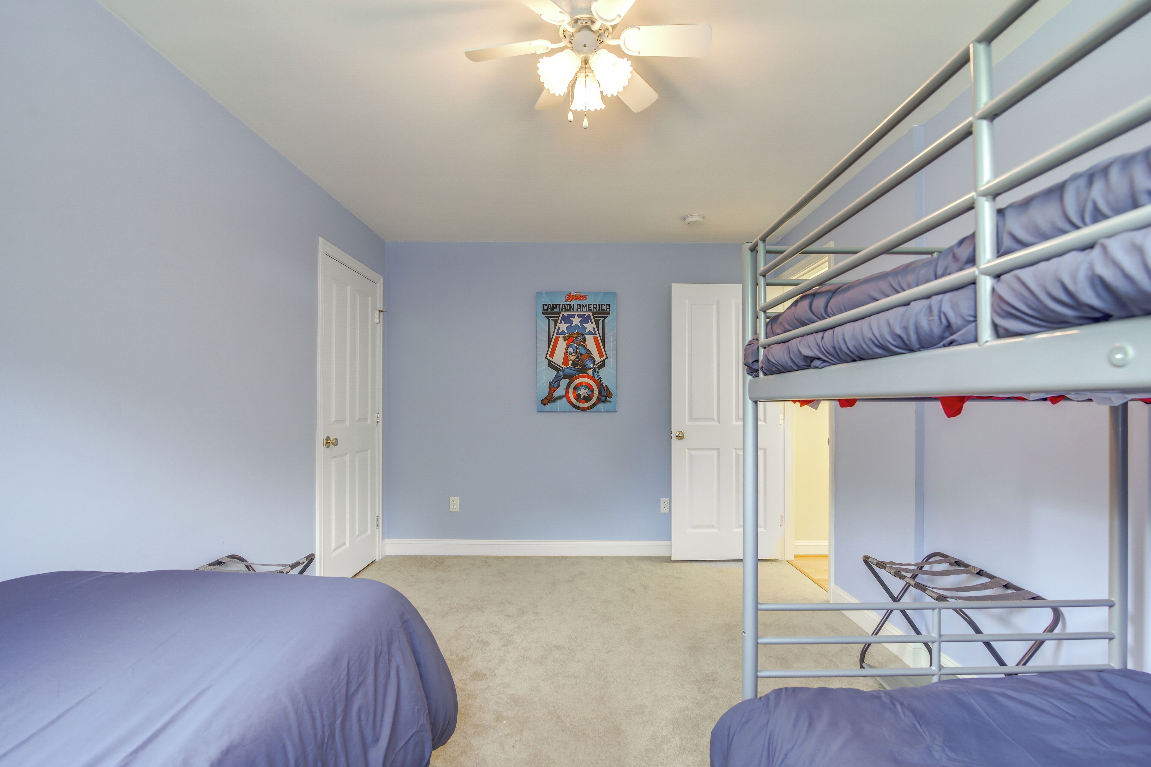 Una habitación con dos camas individuales, una litera, un ventilador de techo y un póster de Capitán América en la pared.