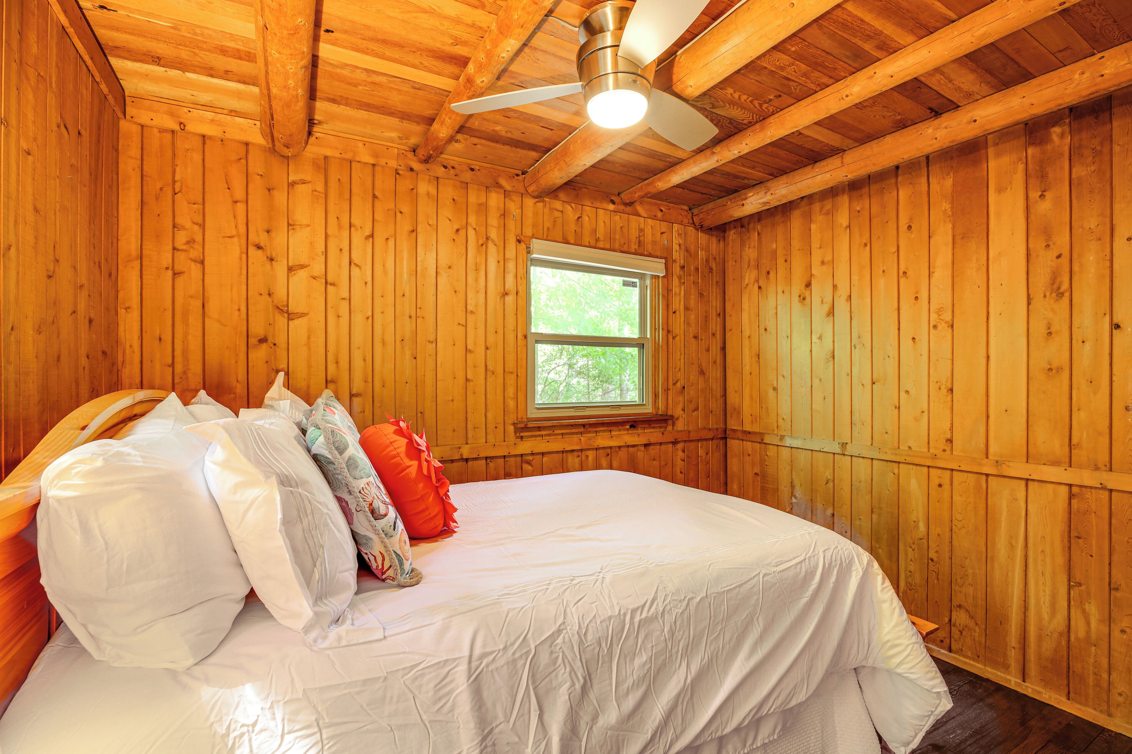 A wooden-paneled room with a bed, a ceiling fan, and a window.
