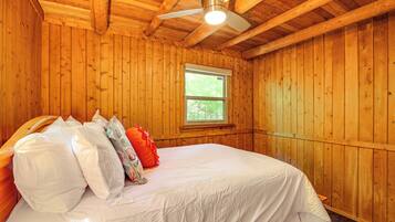 A wooden-paneled room with a bed, a ceiling fan, and a window.
