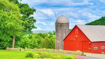 A red barn with a silo, surrounded by lush greenery and a stone wall.
