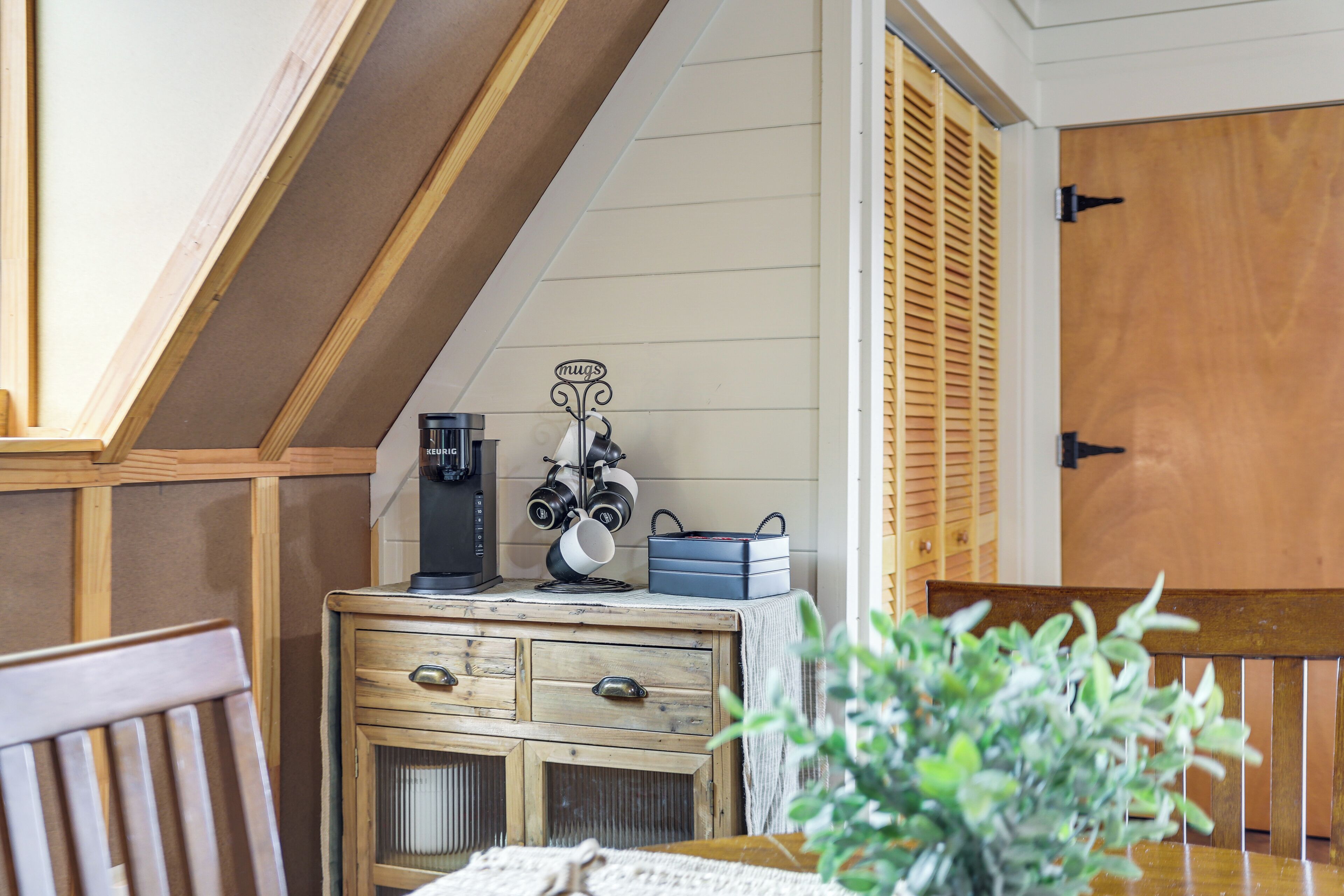 A cozy room with a wooden chest of drawers, a coffee maker, and a mug rack.