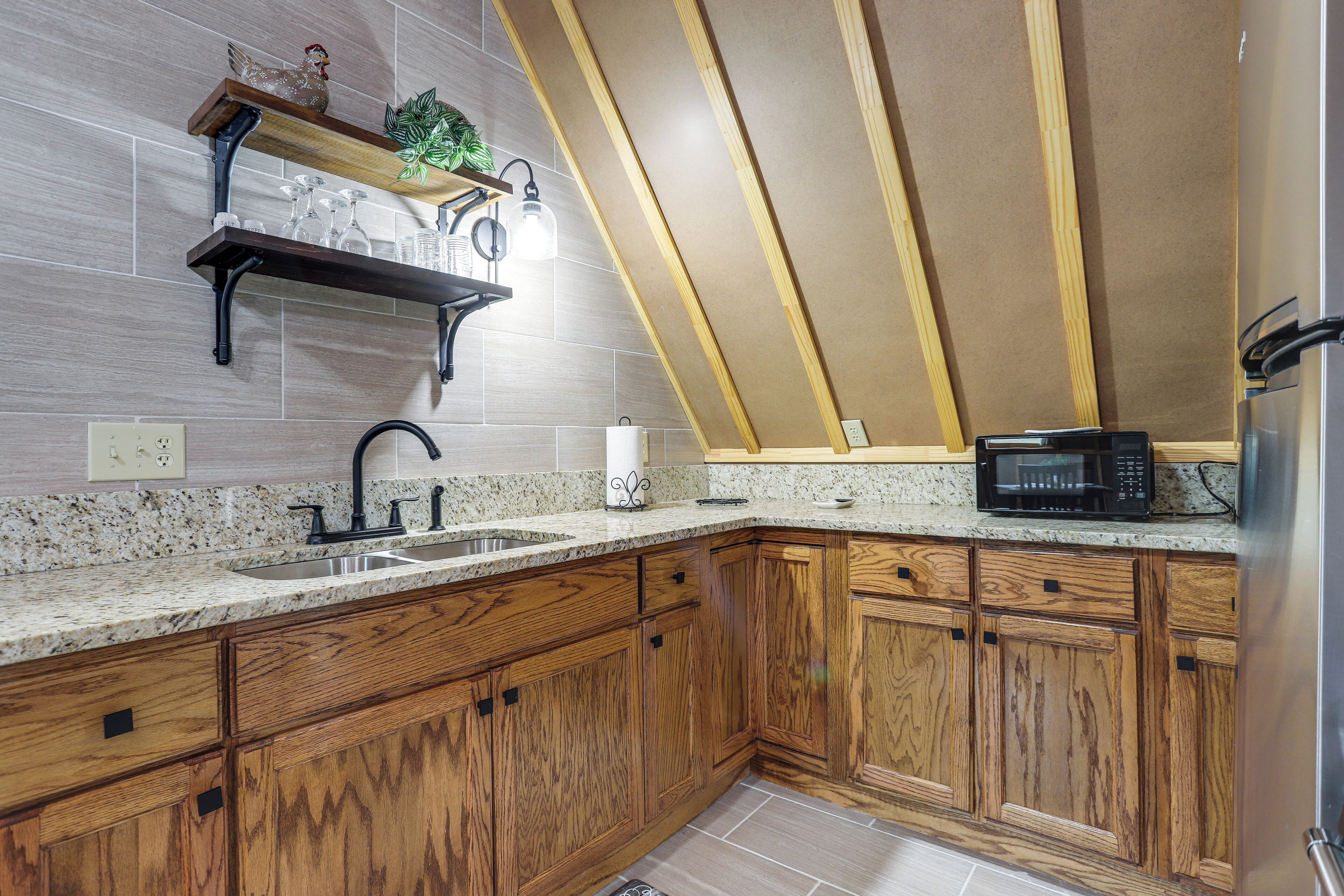 A kitchen with wooden cabinets, a granite countertop, a stainless steel sink, a microwave, and a wooden ceiling beam structure.