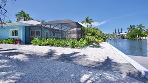 A modern building with a covered outdoor area, a waterfront view, and a gravel pathway. - 🦩Canal Front Home with Covered, Private Pool-Flamingo Bay🦩 (Fort Myers Beach)
