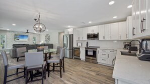 A modern kitchen with white cabinets, stainless steel appliances, and a dining area with a glass table and chairs. - 🦩Canal Front Home with Covered, Private Pool-Flamingo Bay🦩 (Fort Myers Beach)