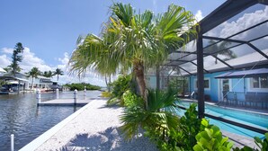 A pool area with a palm tree, a covered seating area, and a view of the water. - 🦩Canal Front Home with Covered, Private Pool-Flamingo Bay🦩 (Fort Myers Beach)