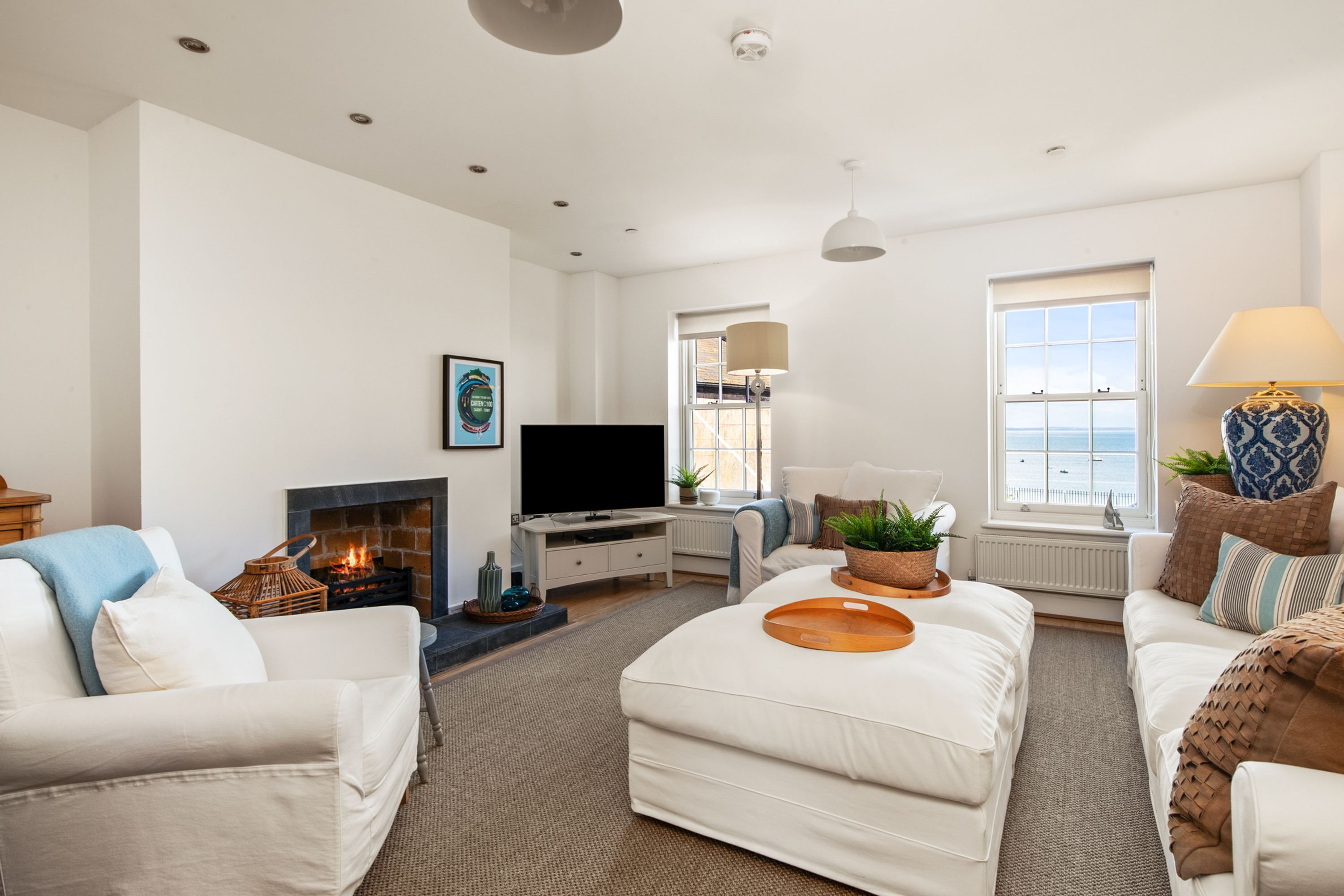 A modern living room with a fireplace, a television, and a large window overlooking the sea.