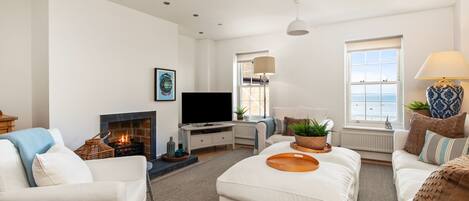 A modern living room with a fireplace, a television, and a large window overlooking the sea.