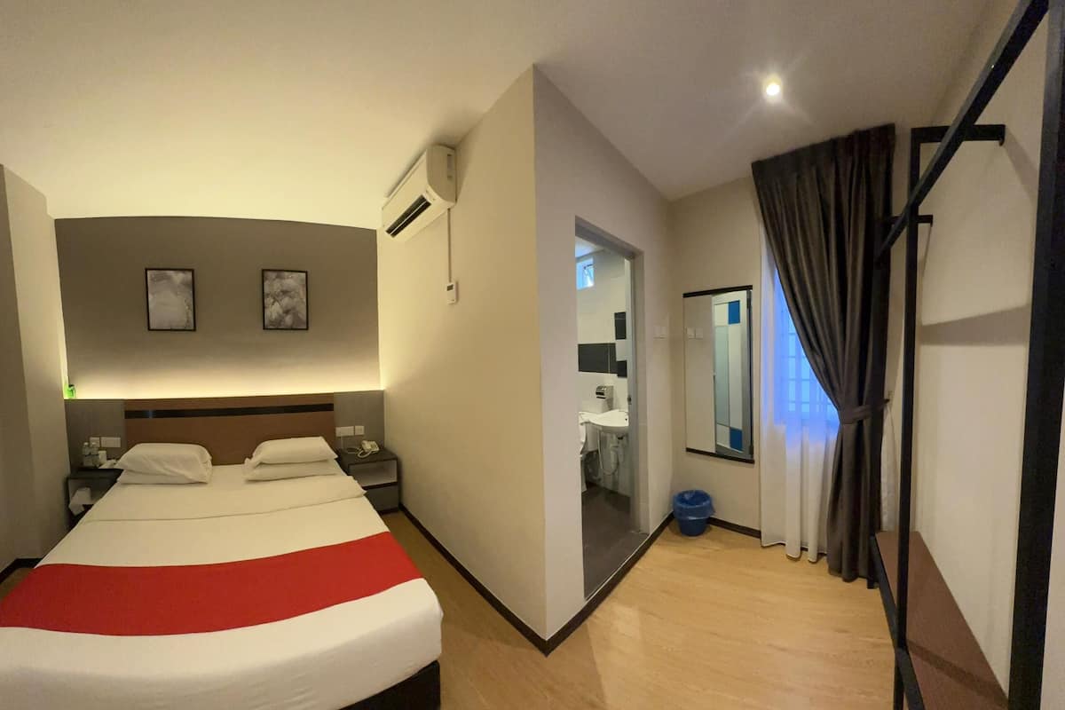 Ein Hotelzimmer mit einem großen Bett, Nachttischen, einem Spiegel, einem Fenster mit Vorhängen und einer Klimaanlage.