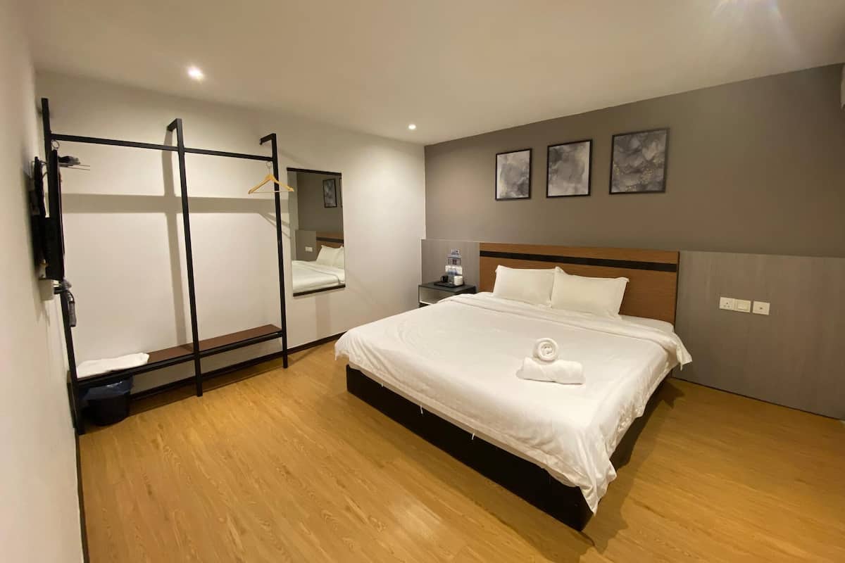 Ein modernes Hotelzimmer mit einem großen Bett, einem begehbaren Kleiderschrank und einem Nachttisch mit Lampe.