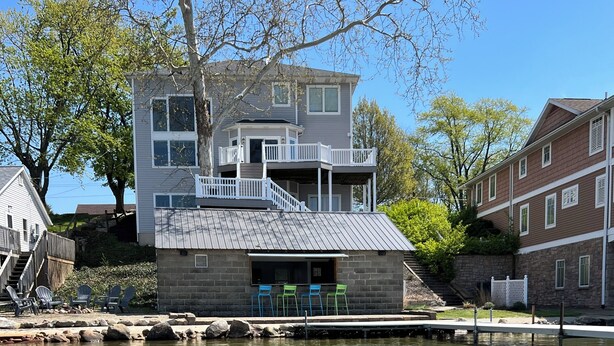 A two-story house with a stone foundation, a balcony, and a dock extending into a clear lake. - Spacious House + boat house on clear, sandy-bottom lake. Arcade + Billiards room (Wolcottville)