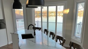 A kitchen with a large island, pendant lights, and a view of a lake through large windows. - Spacious House + boat house on clear, sandy-bottom lake. Arcade + Billiards room (Wolcottville)