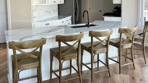 A modern kitchen with white cabinetry, a central island with bar stools, and pendant lighting. - Spacious House + boat house on clear, sandy-bottom lake. Arcade + Billiards room (Wolcottville)