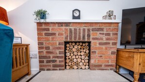 A fireplace with a brick surround, a clock above it, and a TV on the wall to the right. - Hawthorn View: Bristol Large House STAE-Homes (Bradley Stoke)