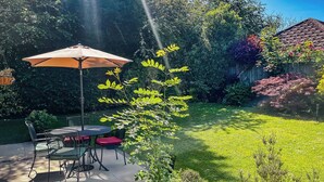 A patio with a table and chairs, surrounded by lush greenery and a wooden fence. - Hawthorn View: Bristol Large House STAE-Homes (Bradley Stoke)