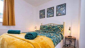 A bed with a patterned bedspread, a rolled towel, and a bedside lamp. - Hawthorn View: Bristol Large House STAE-Homes (Bradley Stoke)