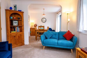 Un salon avec un canapé bleu, un meuble en bois, une table à manger et une horloge au mur.