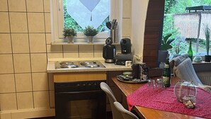 Una cocina con ventana, una mesa de comedor con sillas, lavavajillas y suelo de baldosas.