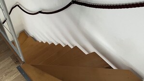 Una escalera de madera con una pared blanca y un descansillo cubierto de alfombra marrón.