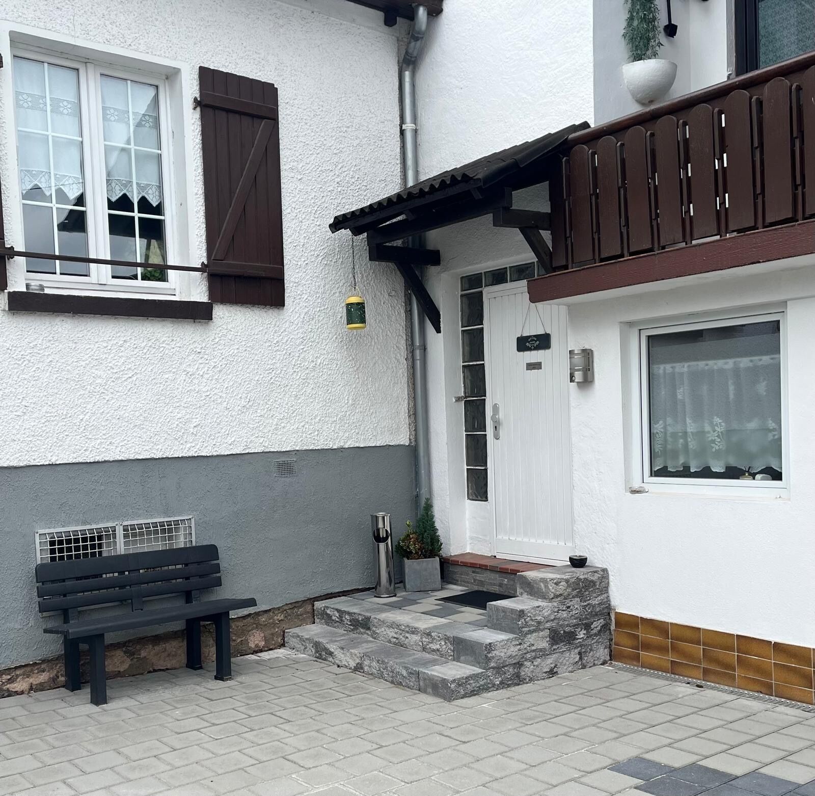 Ein weißes Gebäude mit einem hölzernen Balkon, einer Bank und einem kleinen Garten.
