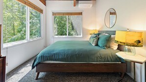 A bedroom with a bed, two windows, a bedside lamp, and a mirror.