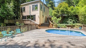 A two-story wooden house with a deck, a swimming pool, and outdoor furniture.