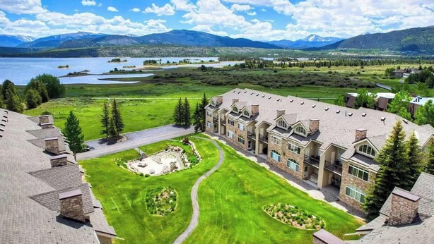 A large, multi-story building with a symmetrical facade, a central courtyard, and a view of a lake and mountains in the background. - Beaver Lodge — 2BR Frisco Condo, Walk to Lake Dillon, Hot Tub, Sleeps 5 (Frisco)