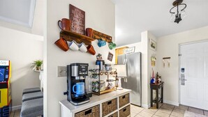 A kitchen with a coffee machine, mugs on a wall-mounted rack, a refrigerator, and a coffee bar. - Top Rated Condo | Mtn Views- POOL- Playground (Pigeon Forge)