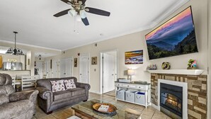 A living room with a fireplace, a sofa, a coffee table, and a TV mounted on the wall. - Top Rated Condo | Mtn Views- POOL- Playground (Pigeon Forge)