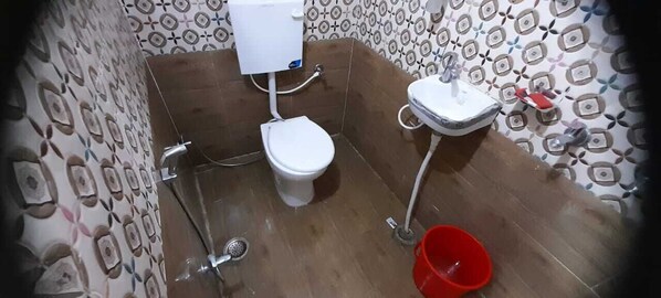 A bathroom with a toilet, sink, and red bucket. - Shiv Kashi Lawn And Guest House (Varanasi)