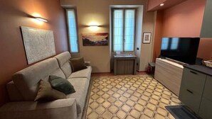Ein gemütlicher Wohnbereich mit Sofa, Fernseher, Schrank und einem Musterboden.
