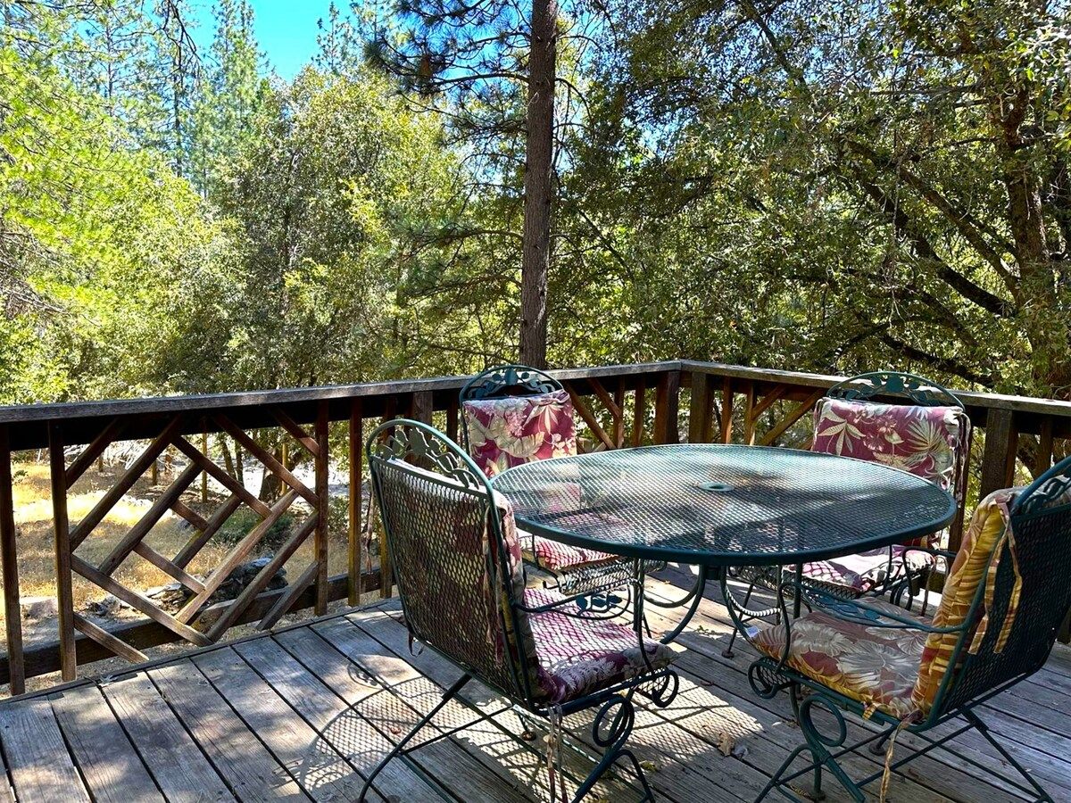 A wooden deck with a metal table and chairs, surrounded by trees.