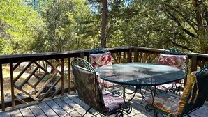 Una terraza de madera con una mesa y sillas de metal, rodeada de árboles.