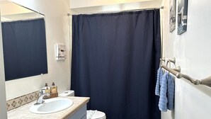 Un baño con un lavamanos blanco, un inodoro, una cortina de ducha azul oscuro y un perchero con toallas.