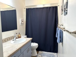 Un baño con un lavamanos blanco, un inodoro, una cortina de ducha azul oscuro y un perchero con toallas.