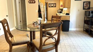 Un comedor con una mesa de vidrio rodeada de sillas de madera, una cocina al fondo y un cubo de basura.