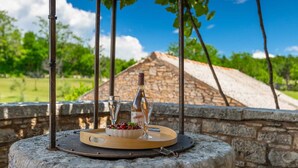 A stone table with a bottle of wine, two glasses, and a bowl of cherries.