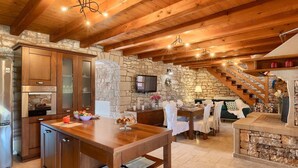 A rustic kitchen with wooden cabinets, a stone wall, and a dining area with a wooden table and chairs.