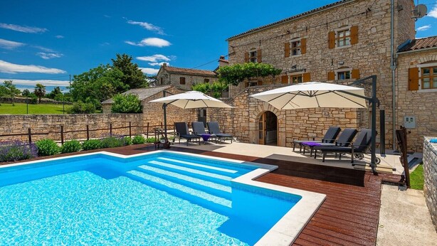 A stone building with a swimming pool, outdoor seating, and umbrellas.